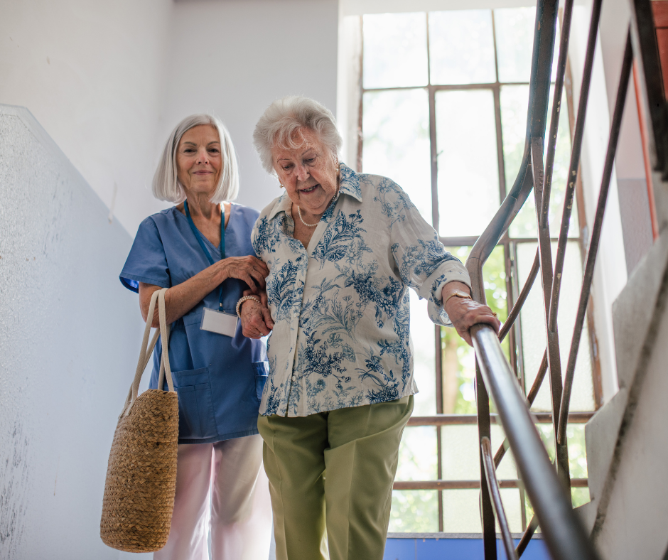 Caregiver assisting an elderly woman down stairs during an in-home primary care visit, illustrating senior healthcare support and aging in place services in Palm Beach County.